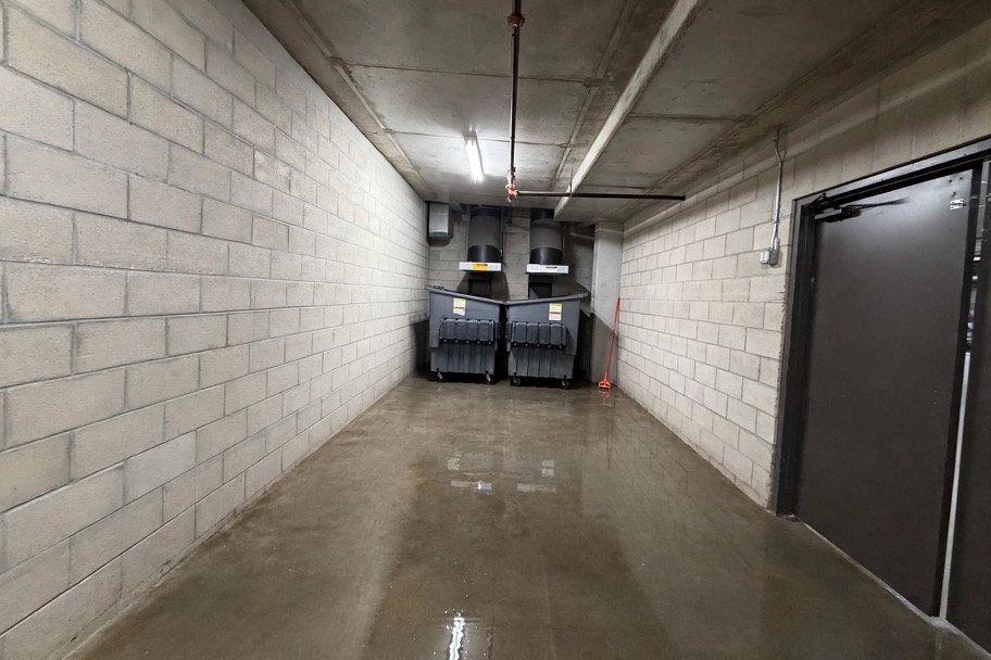 Garage-level trash corridor with a freshly pressure-washed concrete floor