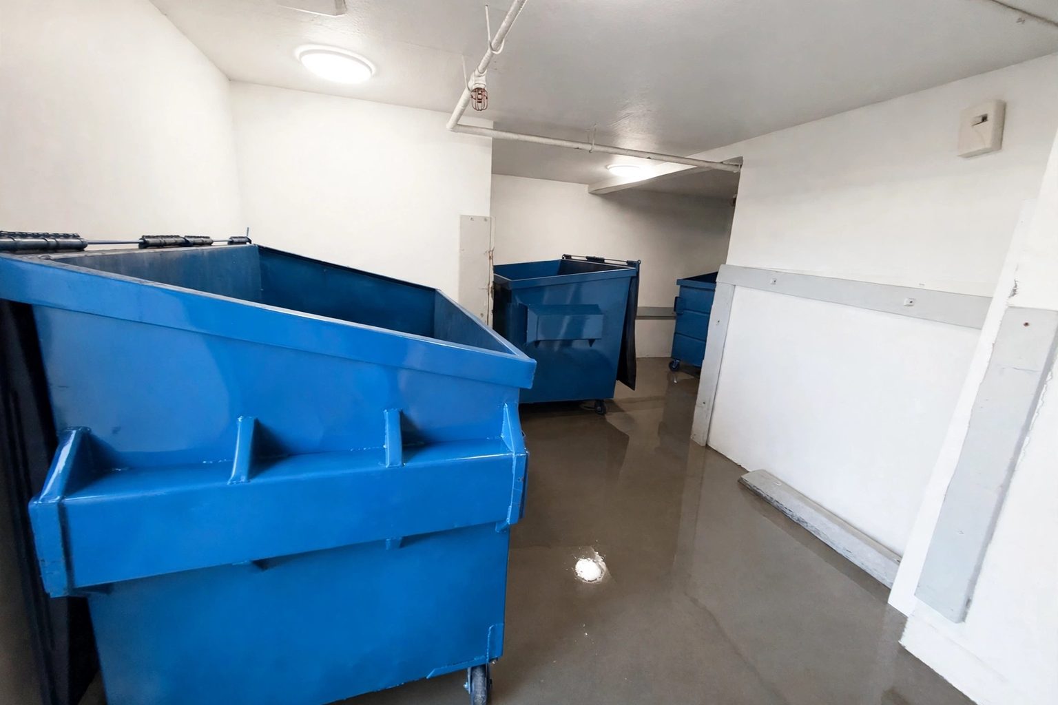 Indoor trash room with dumpsters staged and the floor freshly washed by Bright City